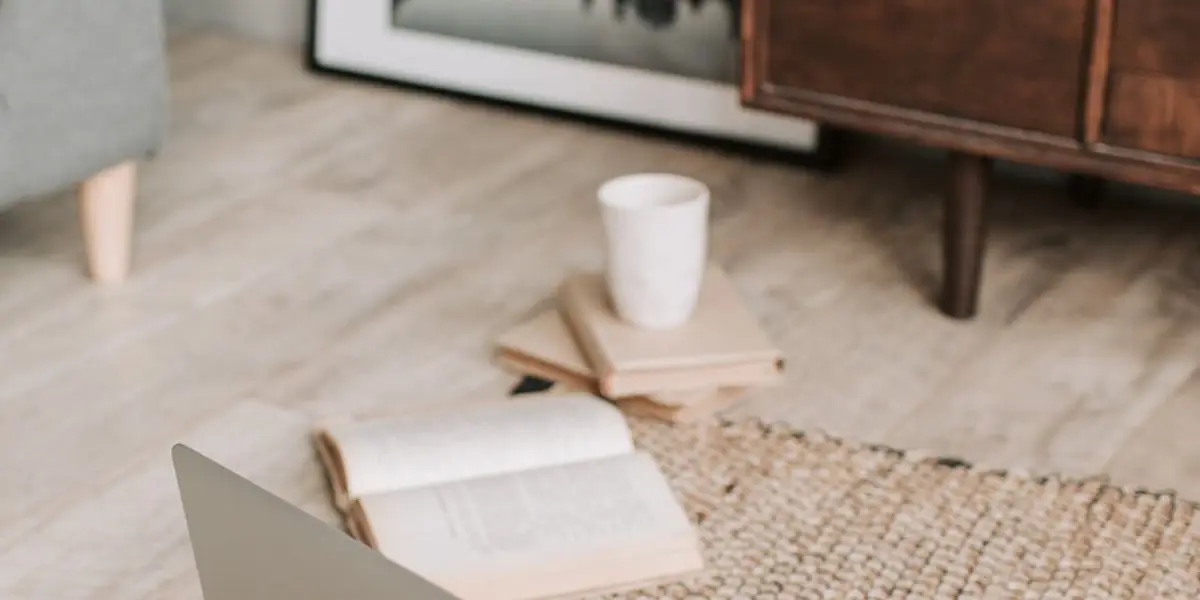 Ein aufgeschlagenes Buch, ein kleiner Bücherstapel und eine Tasse auf einem Teppich in einem Wohnraum