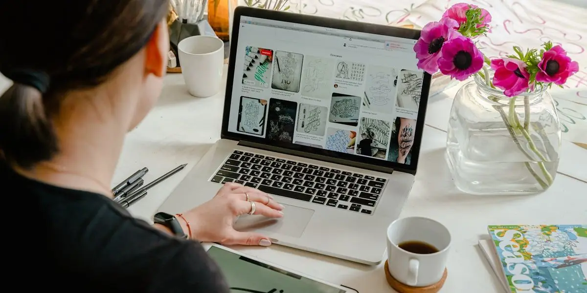 Eine Frau arbeitet am Laptop, daneben Kaffeetasse, Stifte und Blumen auf einem hellen Schreibtisch